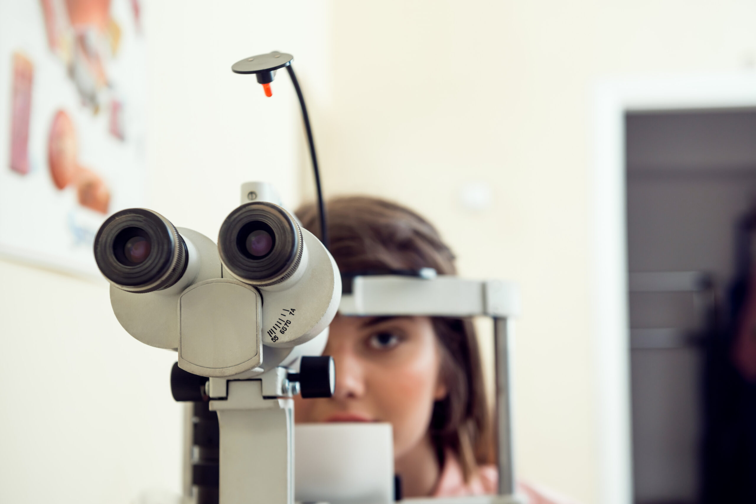 Portrait of cute caucasian female patient sitting in optometrist office, waiting for start of procedure to check her vision with microbioscope, sitting over yellow background. Ophthalmology concept